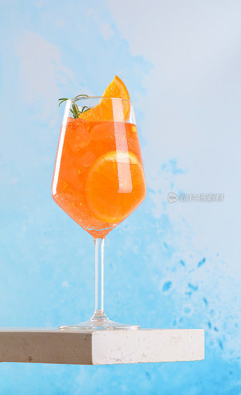 经典的意大利开胃酒aperol spritz鸡尾酒在玻璃与橙色片的蓝色背景，大理石平台